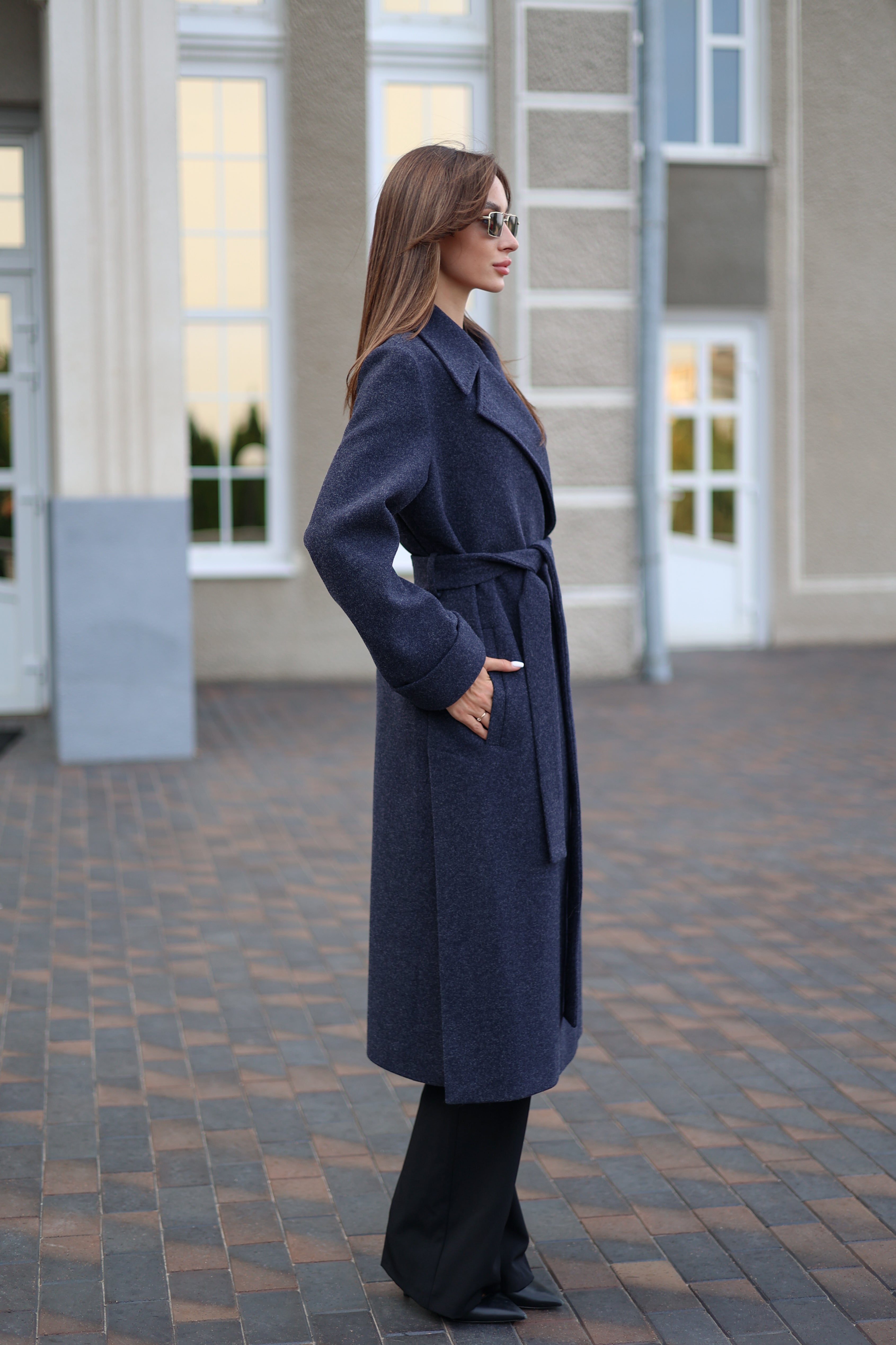 Woman wearing a long navy coat standing on a paved walkway.