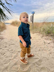 Child standing on a sandy path with beach vegetation and a blue sky in the background