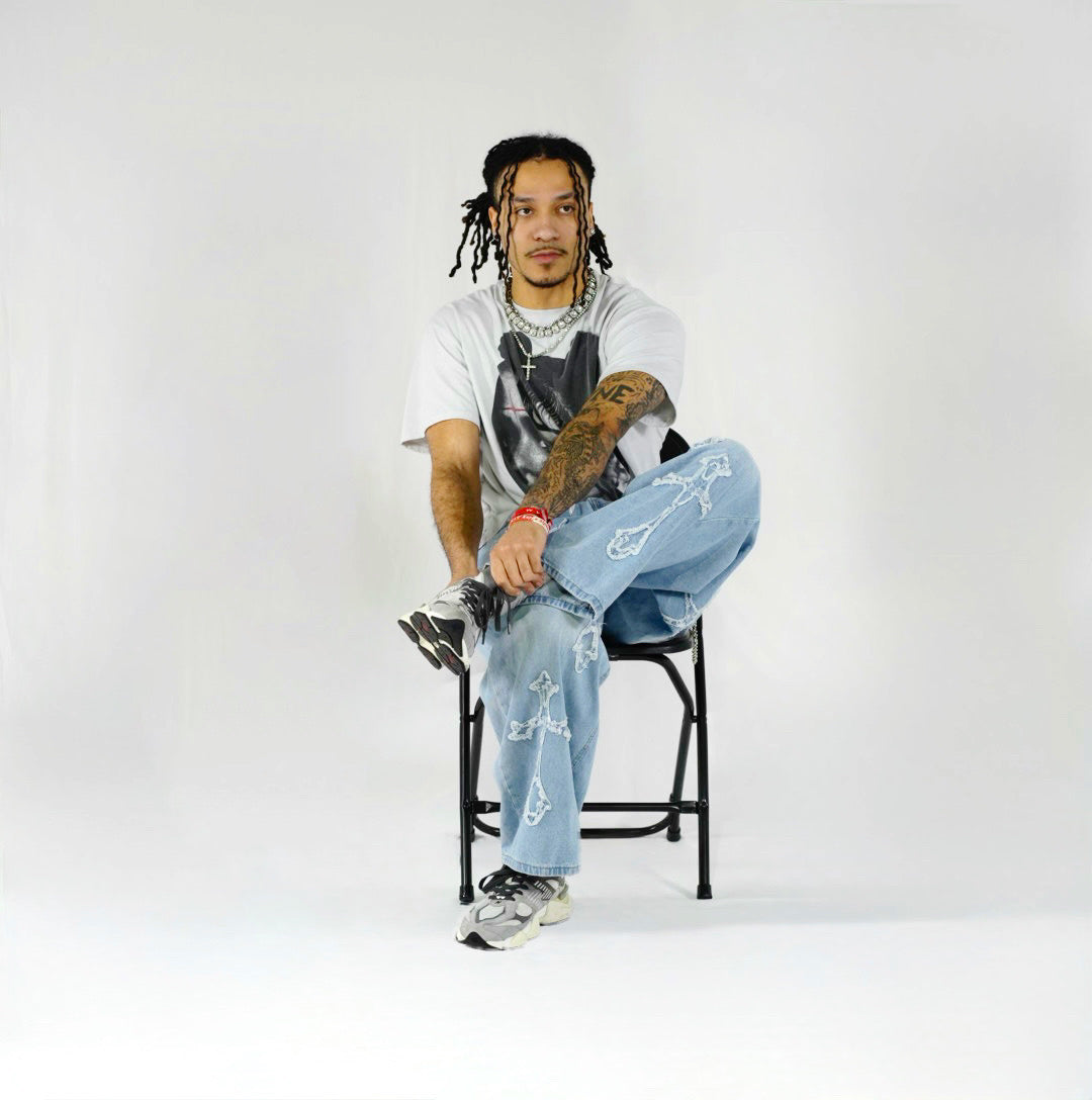 Person sitting on a chair wearing a white t-shirt, blue jeans, and black shoes against a white background