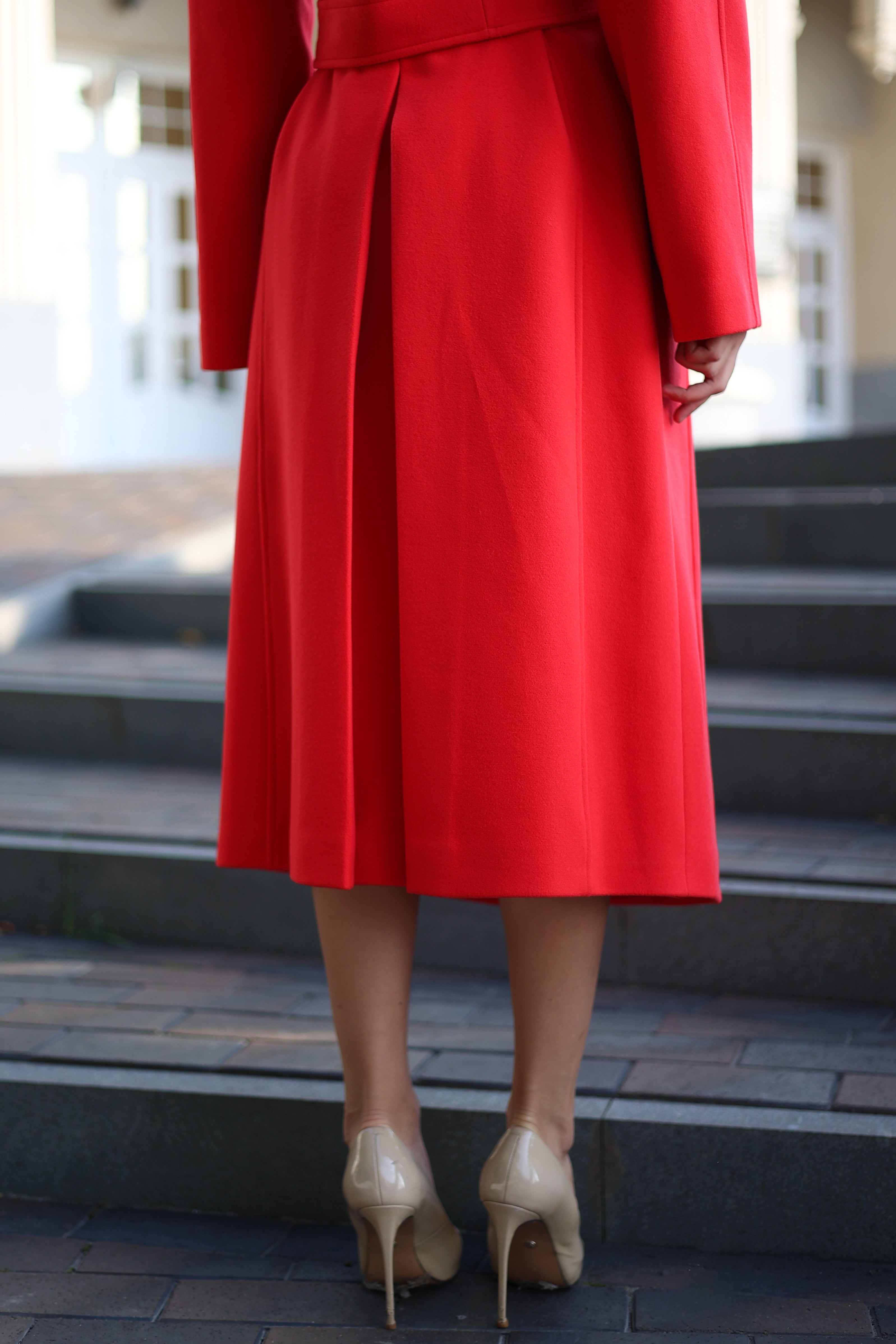 Woman in a red coat and white hat standing on steps outdoors
