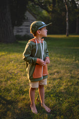 Child wearing a green cap and jacket in a grassy outdoor setting