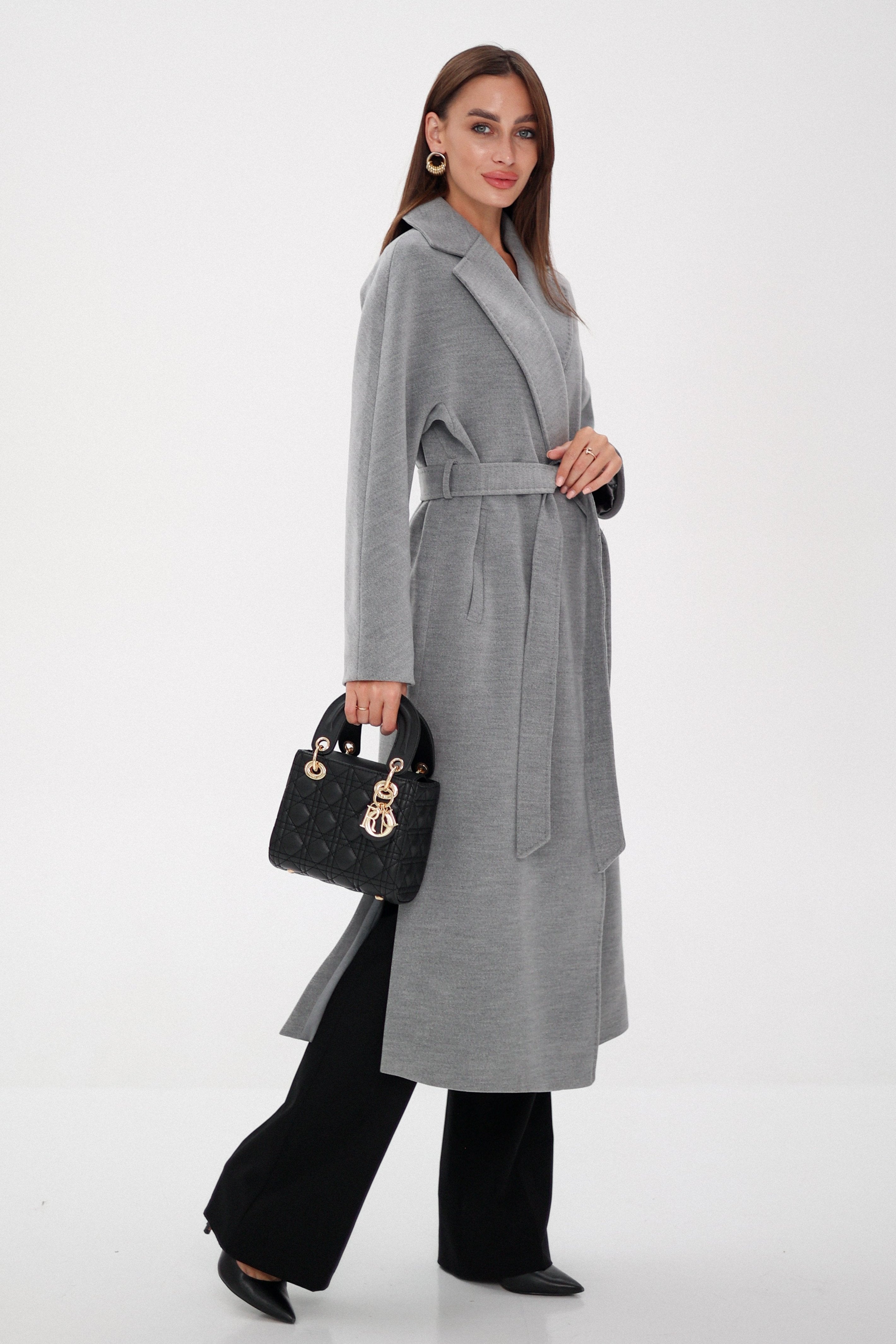 Woman wearing a long gray coat holding a black handbag on a white background