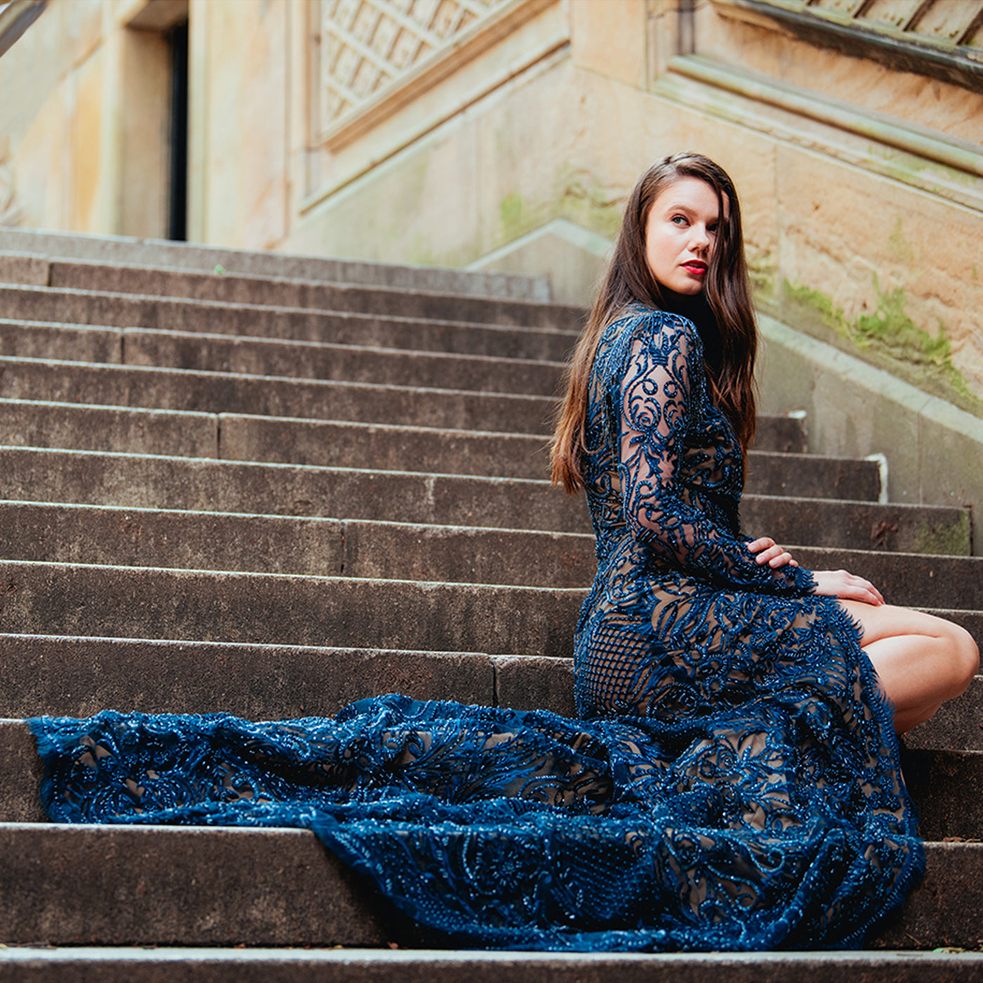 Woman in a blue lace dress sitting on stone steps outdoors.