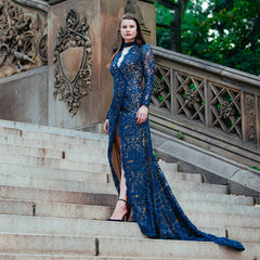 Woman in a blue lace dress standing on stone steps with decorative architecture.