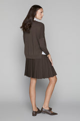 Woman wearing a brown pleated skirt and cardigan on a gray background