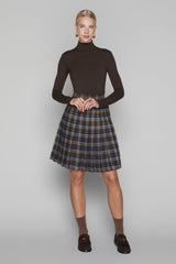 Woman wearing a brown turtleneck and plaid skirt on a gray background