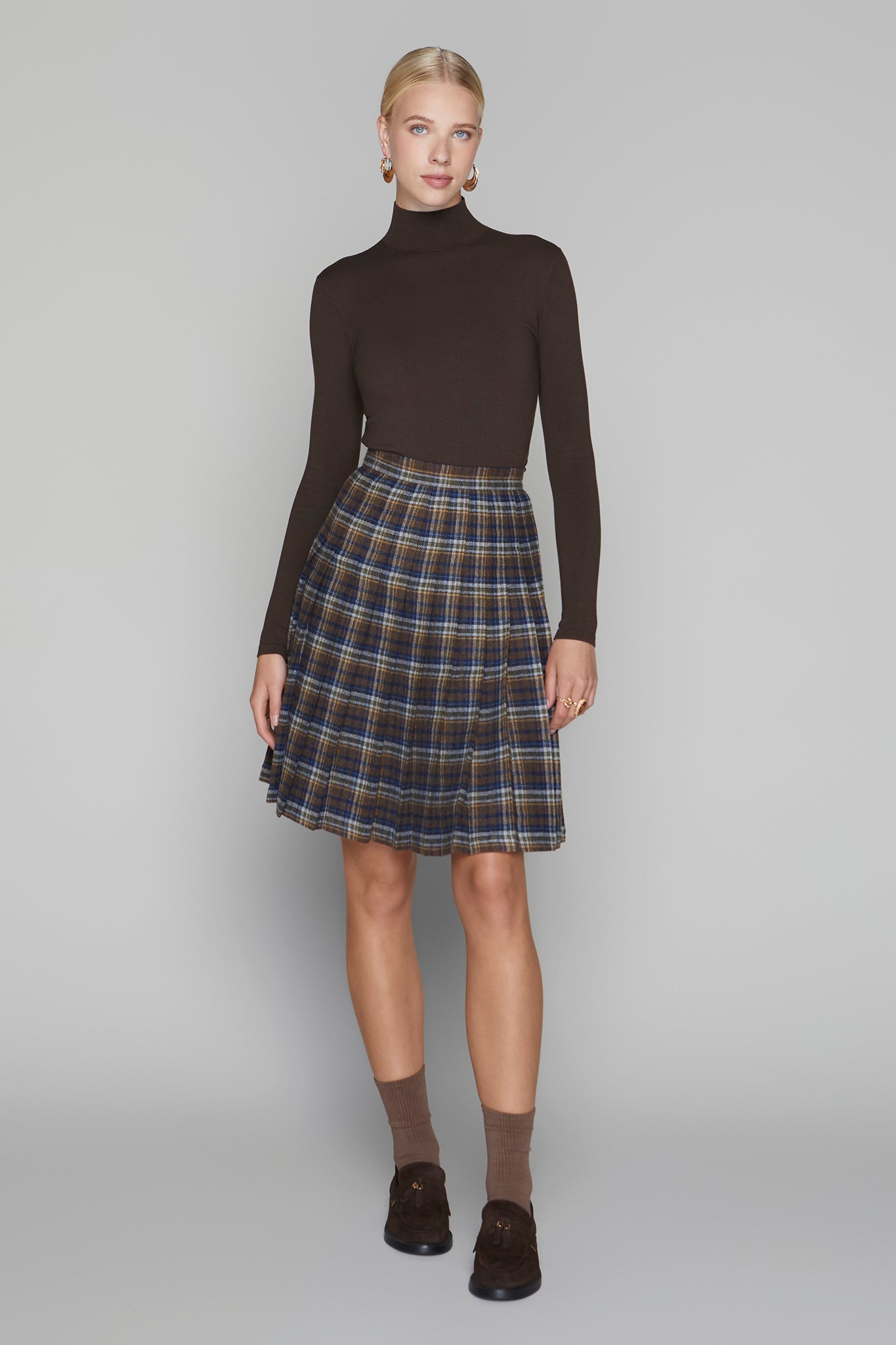 Woman wearing a brown turtleneck and plaid skirt on a gray background
