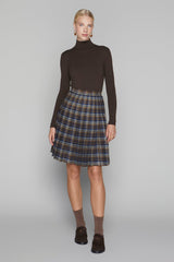 Woman wearing a brown turtleneck and plaid skirt on a gray background