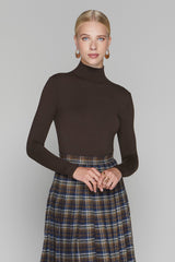 Woman wearing a brown turtleneck and plaid skirt against a plain background