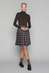 Woman wearing a brown turtleneck and plaid skirt on a gray background