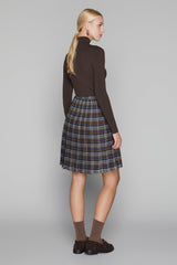 Woman wearing a brown turtleneck and plaid skirt on a gray background