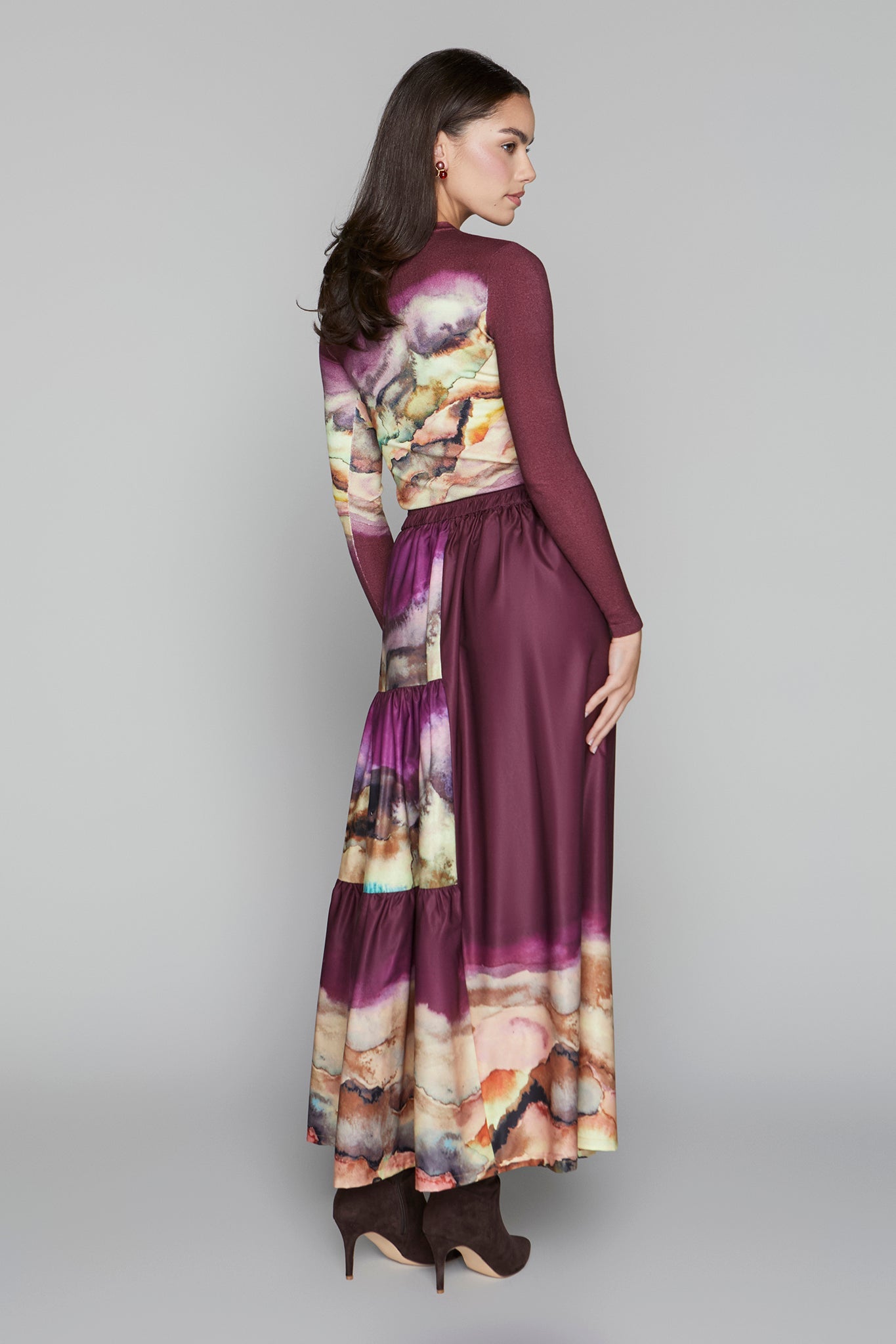 Woman wearing a long, burgundy dress with floral patterns on a gray background
