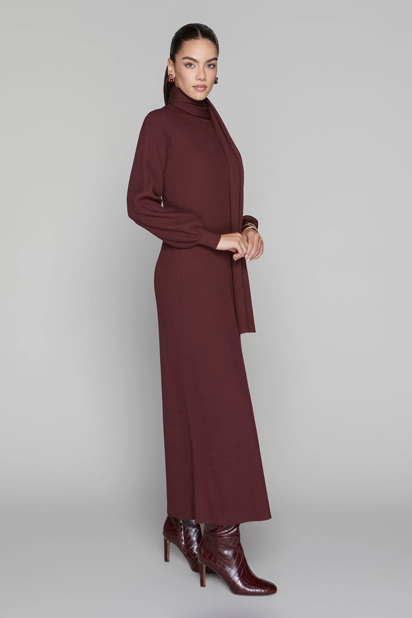 Woman wearing a long burgundy dress with a turtleneck on a gray background
