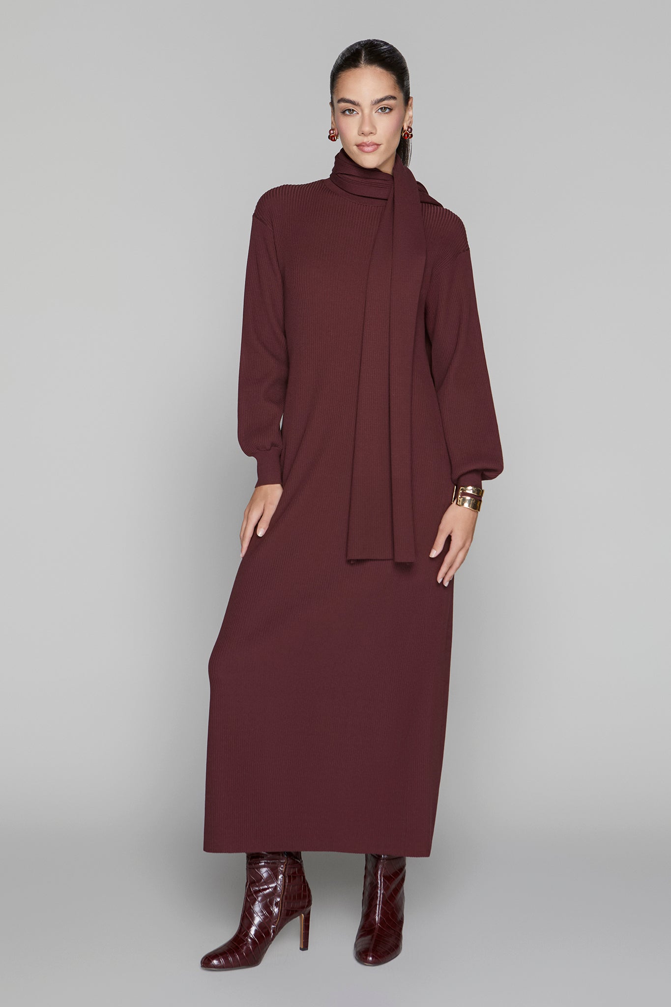 Woman wearing a burgundy dress with a matching cardigan on a gray background