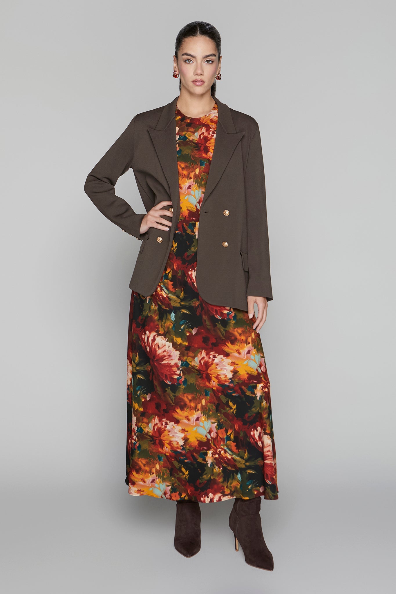 Woman wearing a brown coat over a floral dress on a gray background
