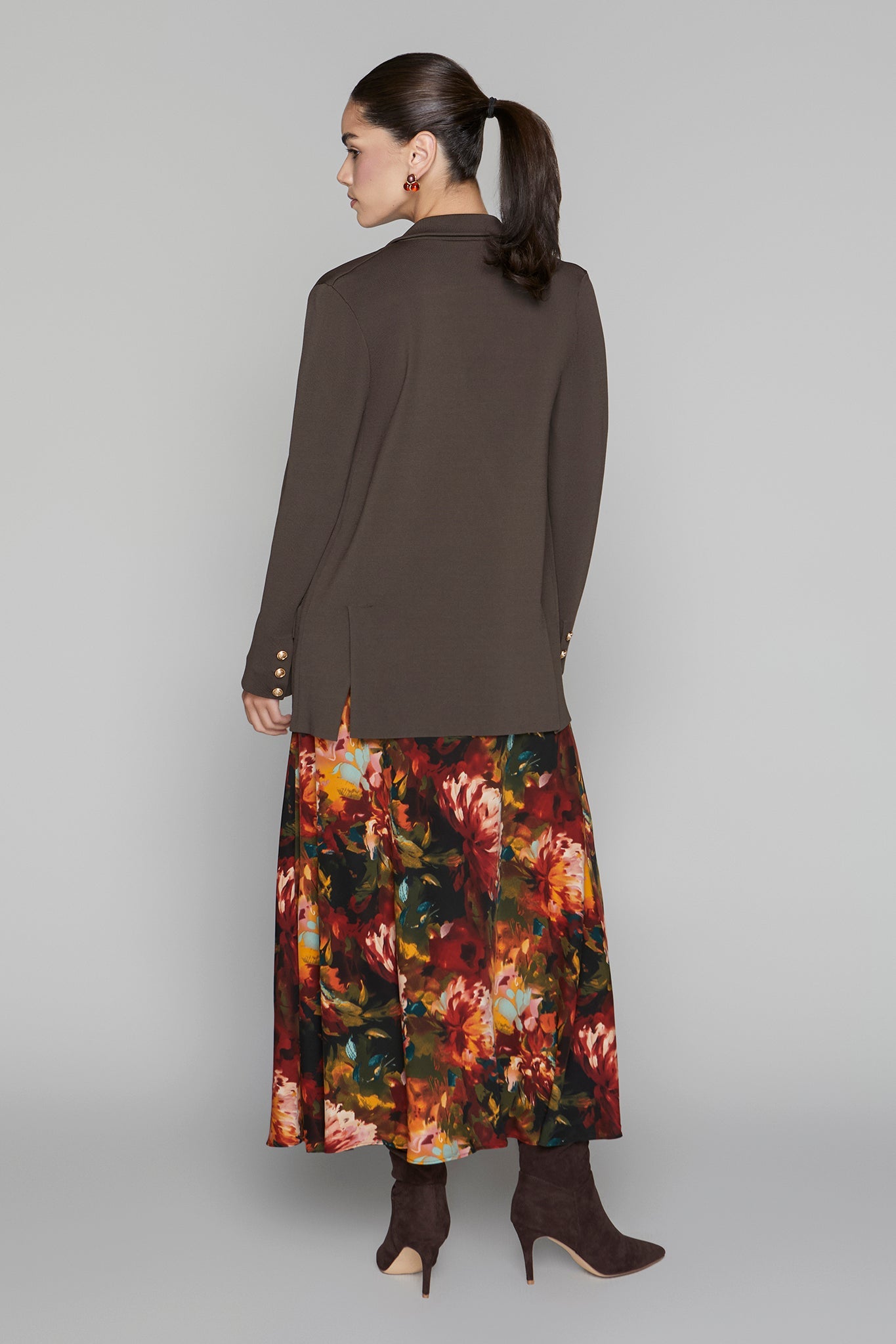 Woman wearing a brown long-sleeve top and a colorful floral skirt on a gray background