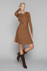 Woman wearing a brown dress with ruffled sleeves and pleated skirt on a gray background