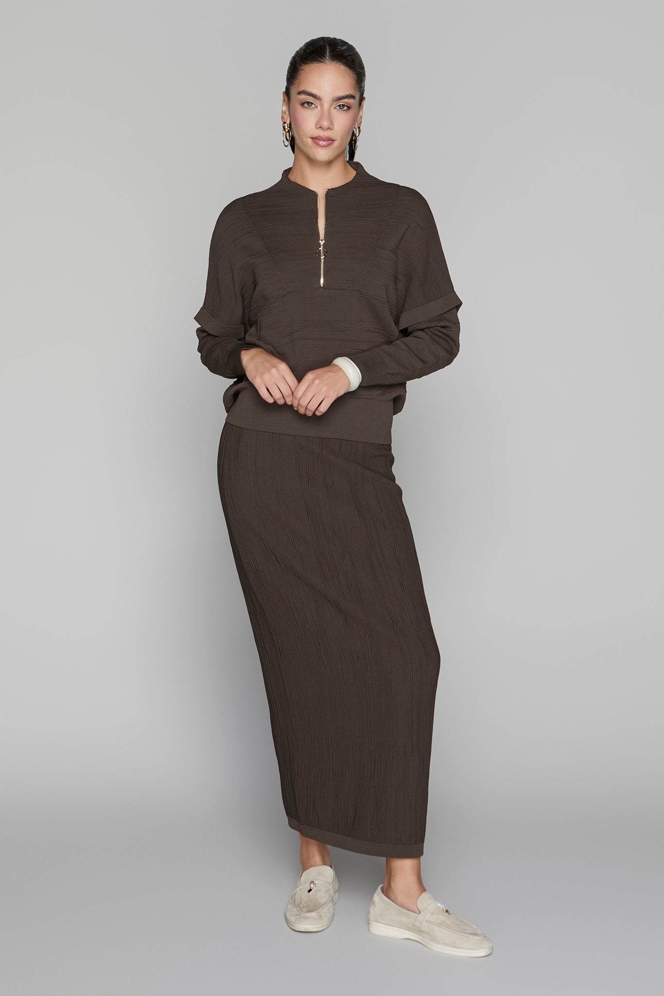 Woman wearing a brown outfit with a long skirt on a gray background