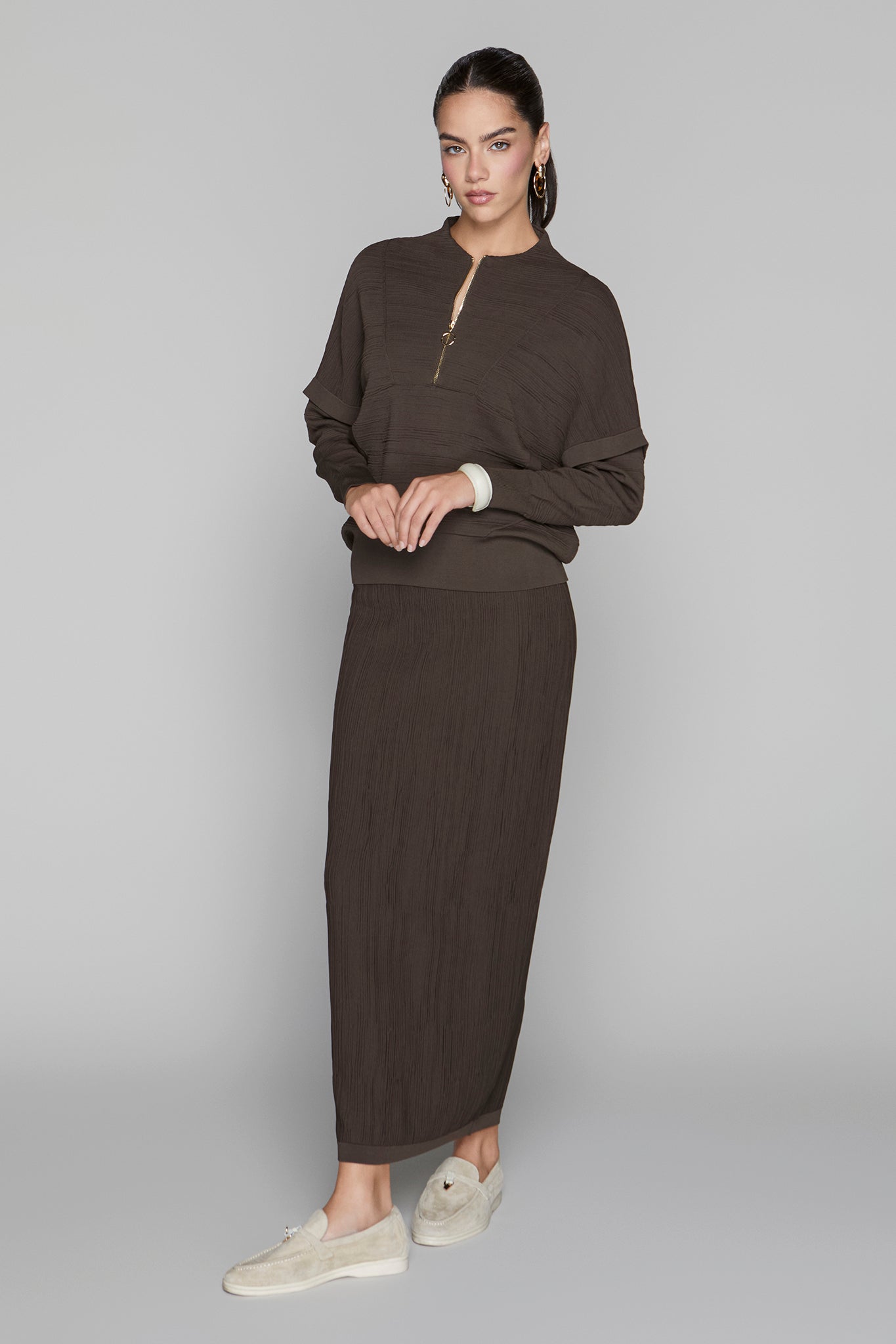 Woman wearing a brown outfit with a long skirt on a gray background