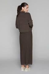 Woman wearing a brown outfit with a long skirt and jacket on a plain background