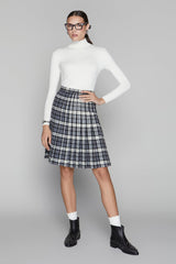 Woman wearing a white turtleneck, plaid skirt, and black boots on a gray background