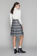Woman wearing a white turtleneck and plaid skirt on a gray background