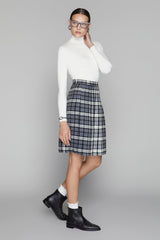 Woman wearing a white turtleneck, plaid skirt, and black boots on a gray background
