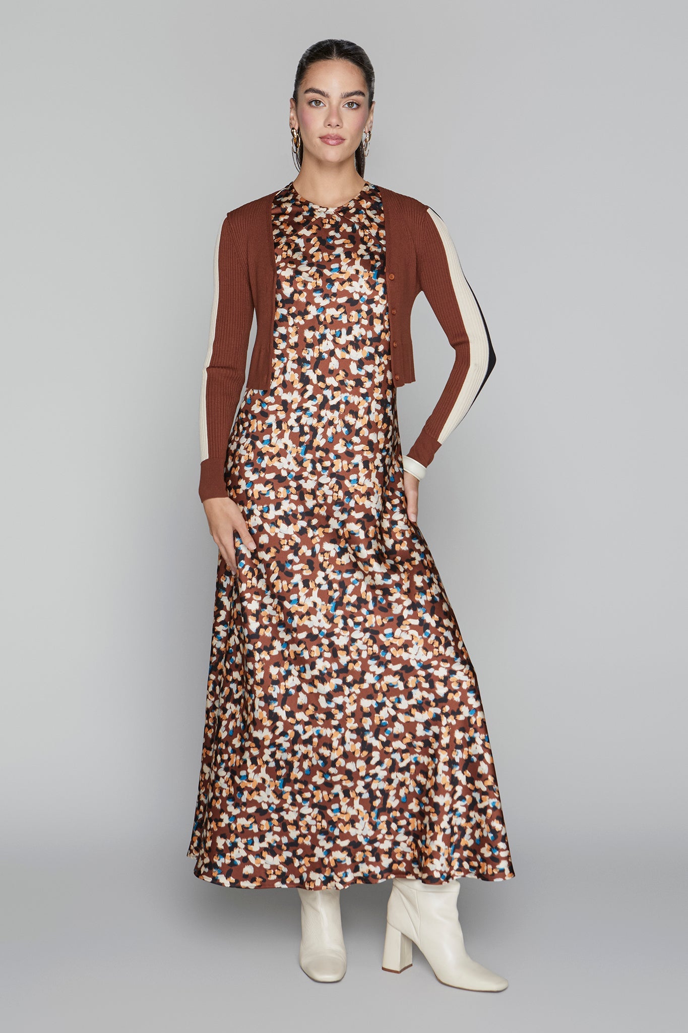 Woman wearing a patterned dress with a brown cardigan on a gray background