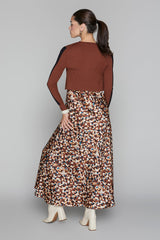 Woman wearing a patterned skirt and brown top on a plain background