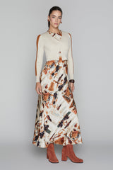 Woman wearing a cream sweater and patterned skirt with red boots on a gray background