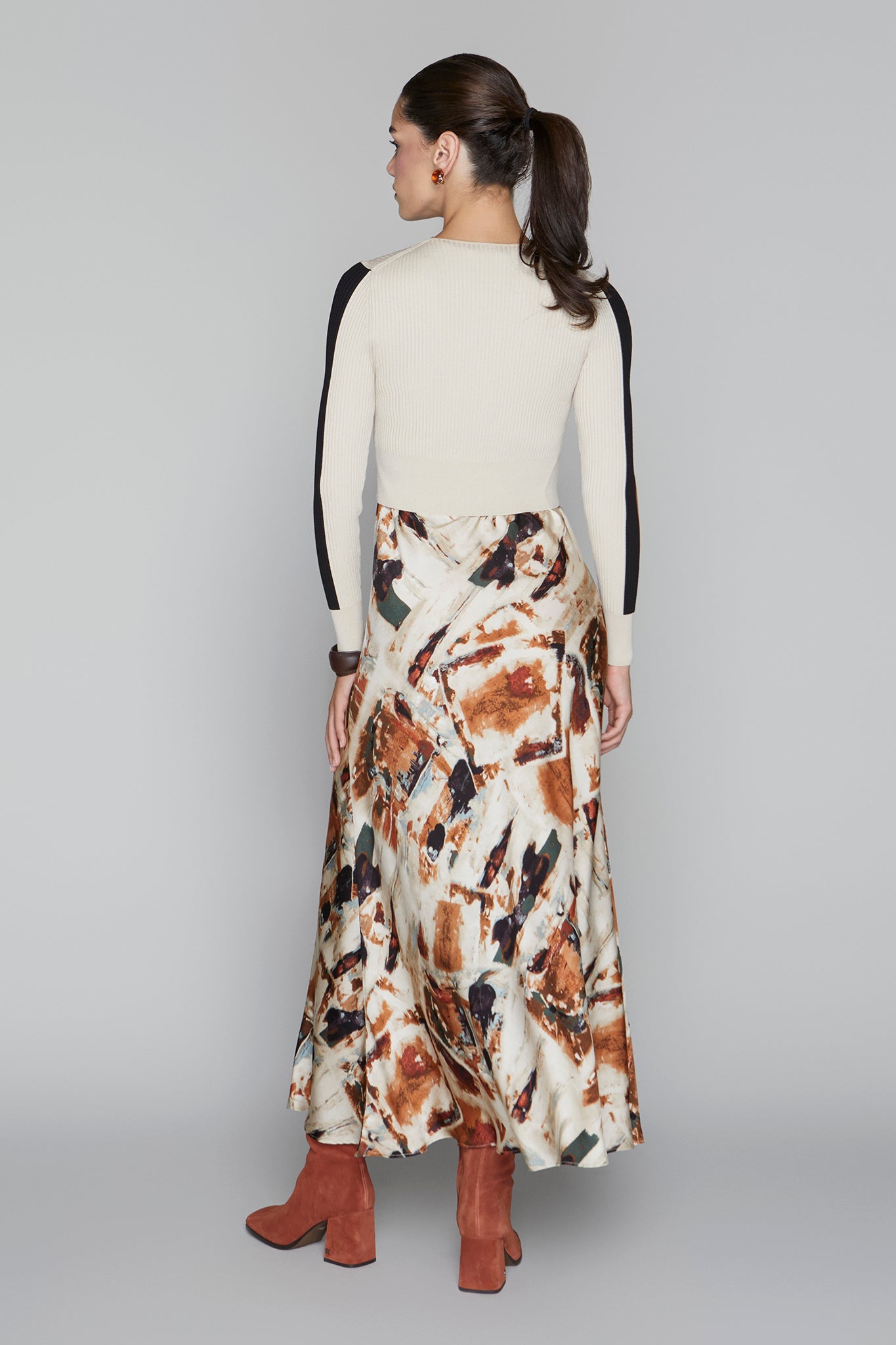 Woman wearing a cream top and patterned skirt on a gray background