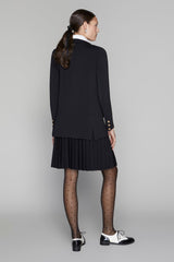 Woman wearing a black blazer and pleated skirt on a gray background