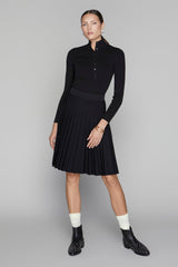 Woman wearing a black long-sleeve top and skirt with white socks and black shoes on a gray background