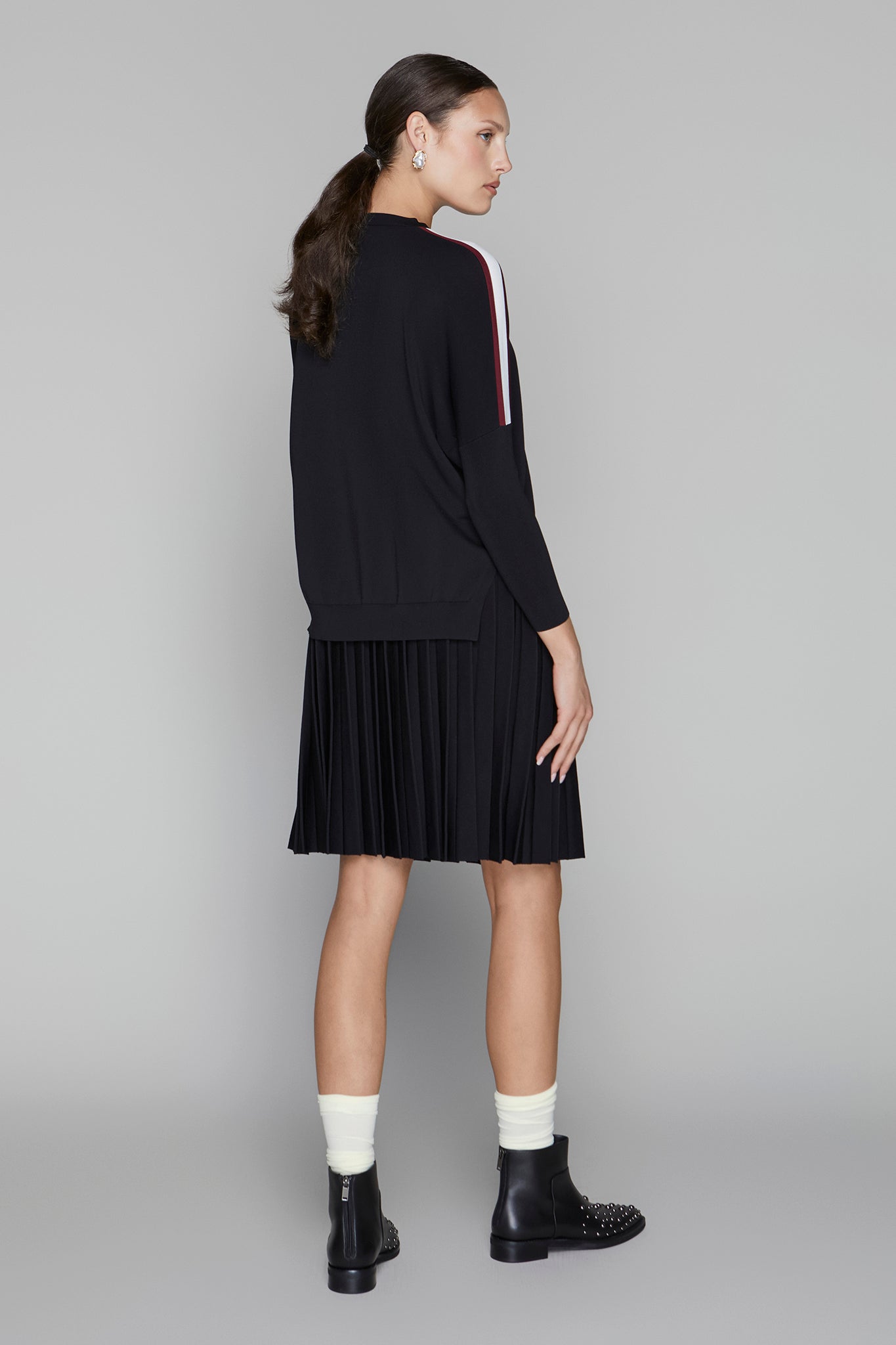 Woman wearing a black dress with white socks and black shoes on a gray background