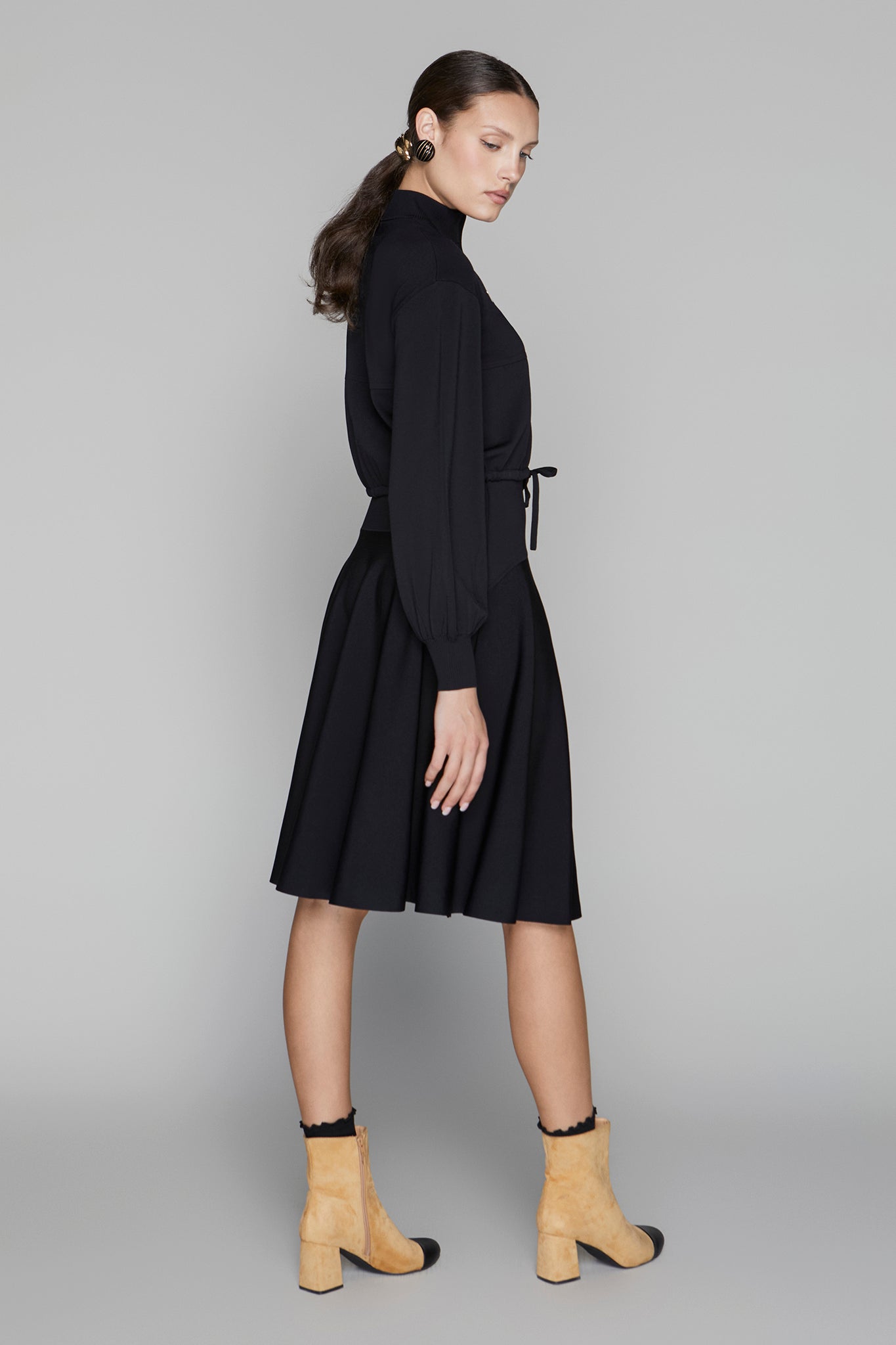 Woman wearing a black dress with yellow boots on a gray background