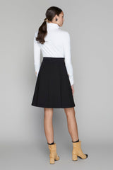 Woman wearing a white turtleneck and black skirt with yellow boots on a gray background