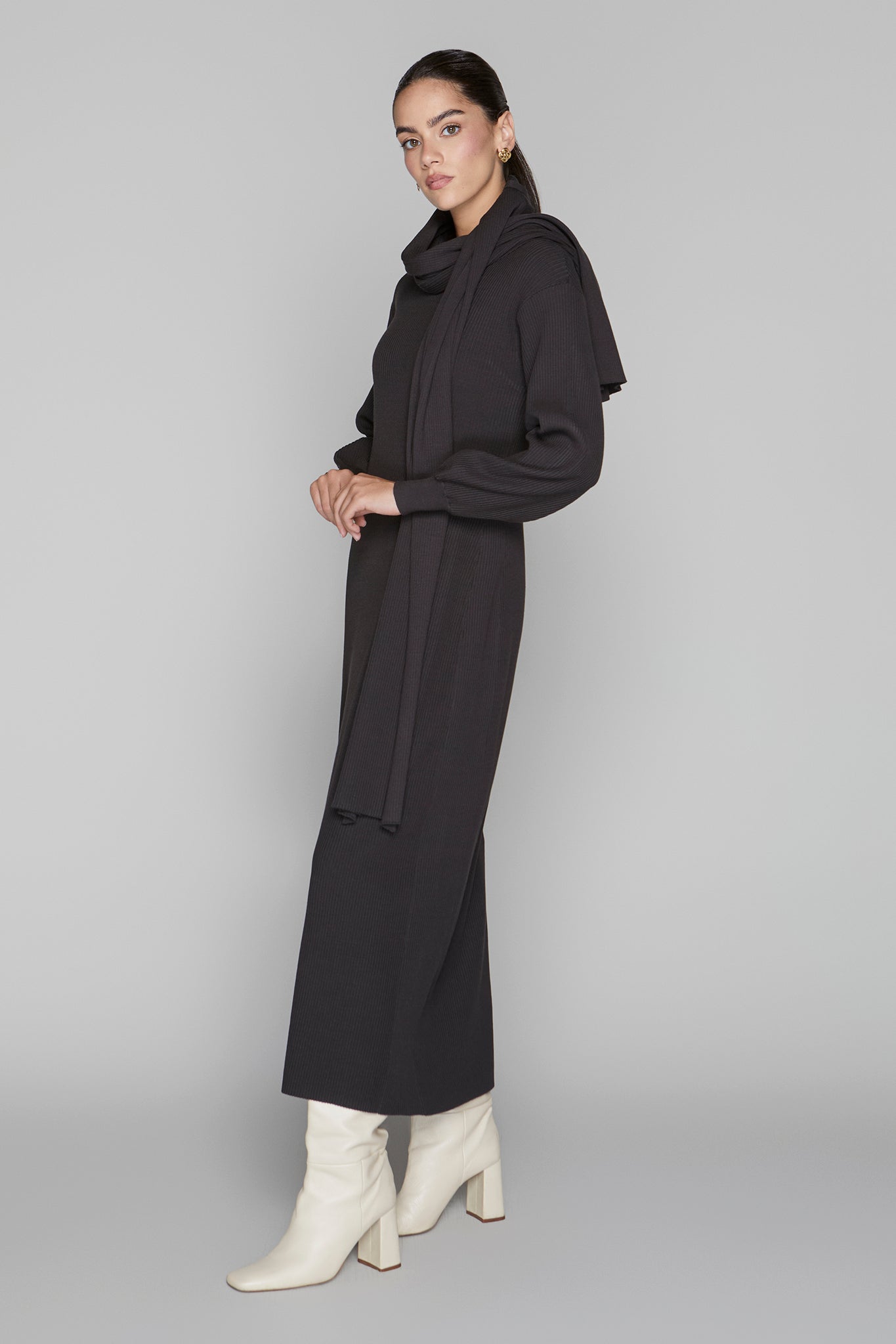 Woman wearing a black outfit with white boots on a gray background