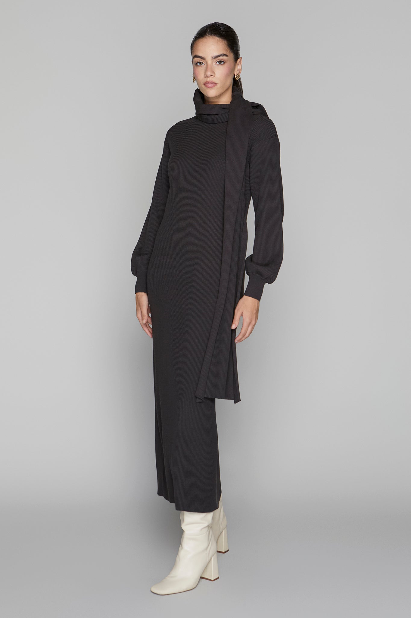 Woman wearing a black dress with a high collar and long sleeves on a gray background