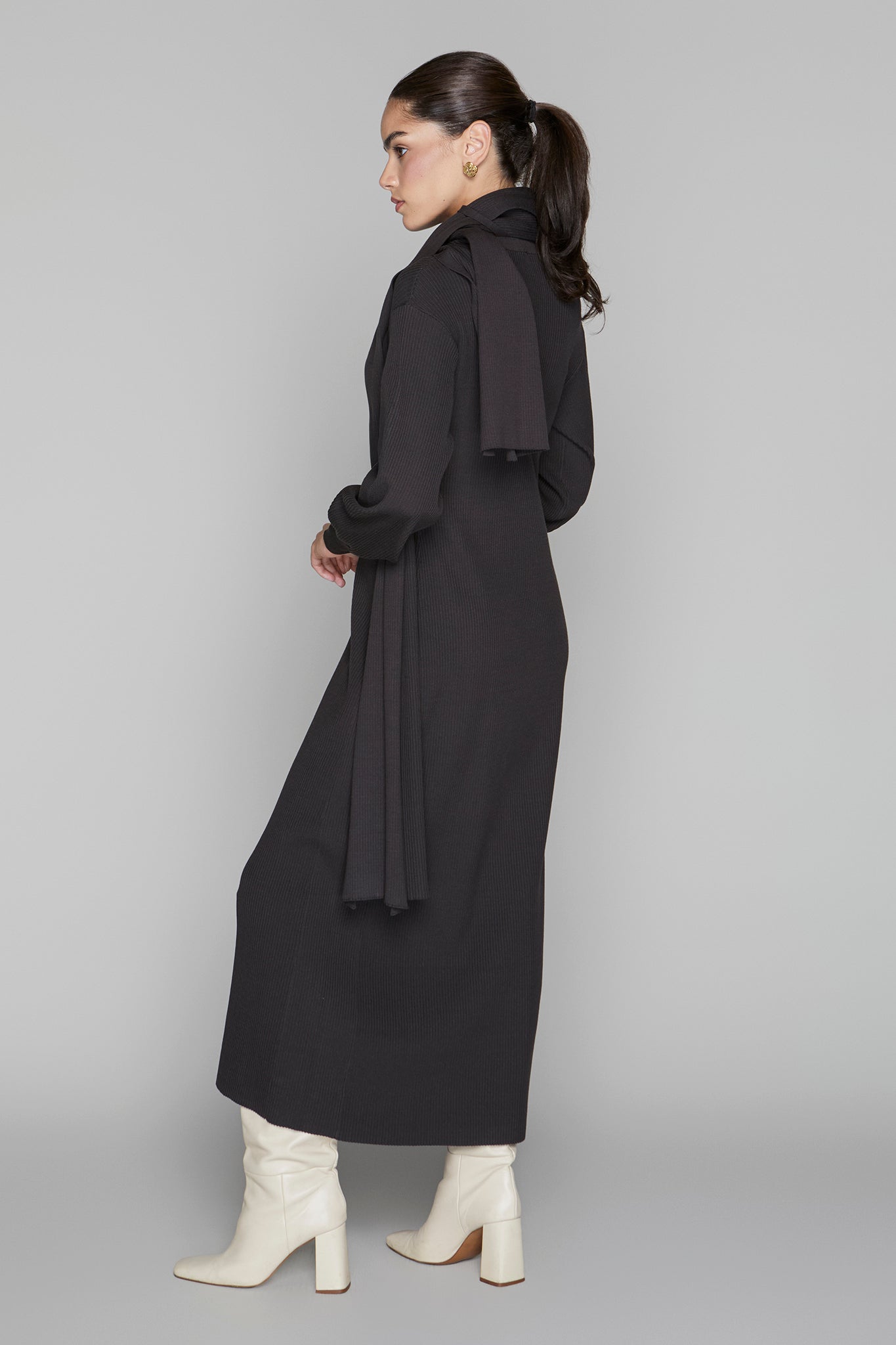 Woman wearing a long black coat on a gray background