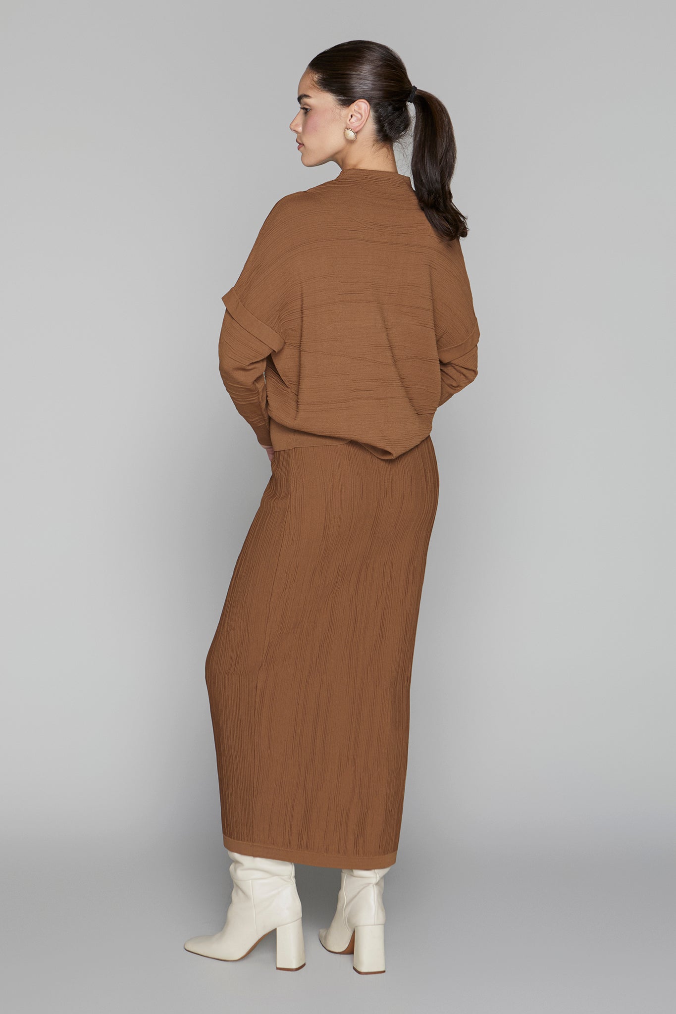 Woman wearing a brown outfit with white boots on a gray background