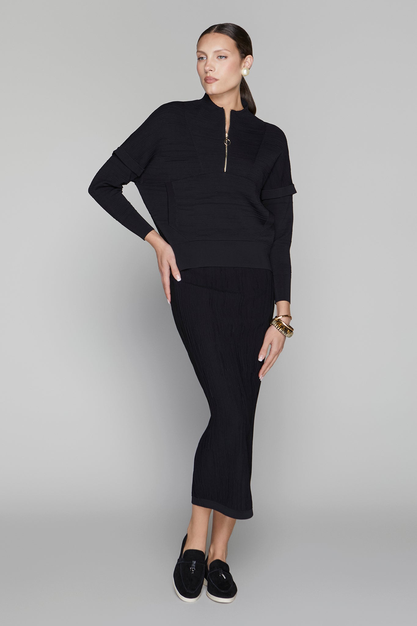 Woman wearing a black outfit with a high-low hem on a gray background