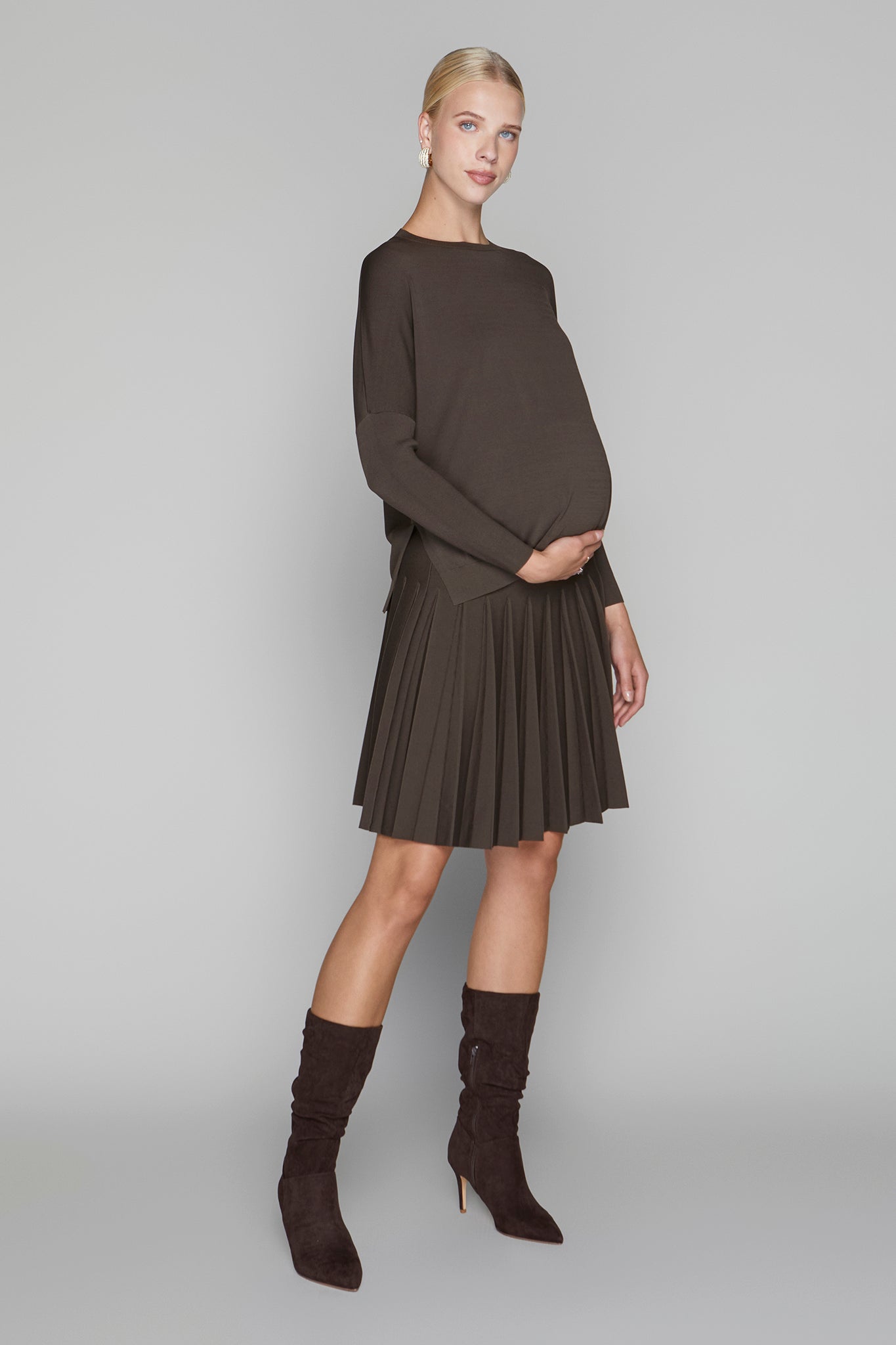 Woman wearing a brown outfit with a sweater and pleated skirt on a gray background