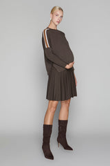 Woman wearing a brown dress with a pleated skirt and matching knee-high boots on a gray background