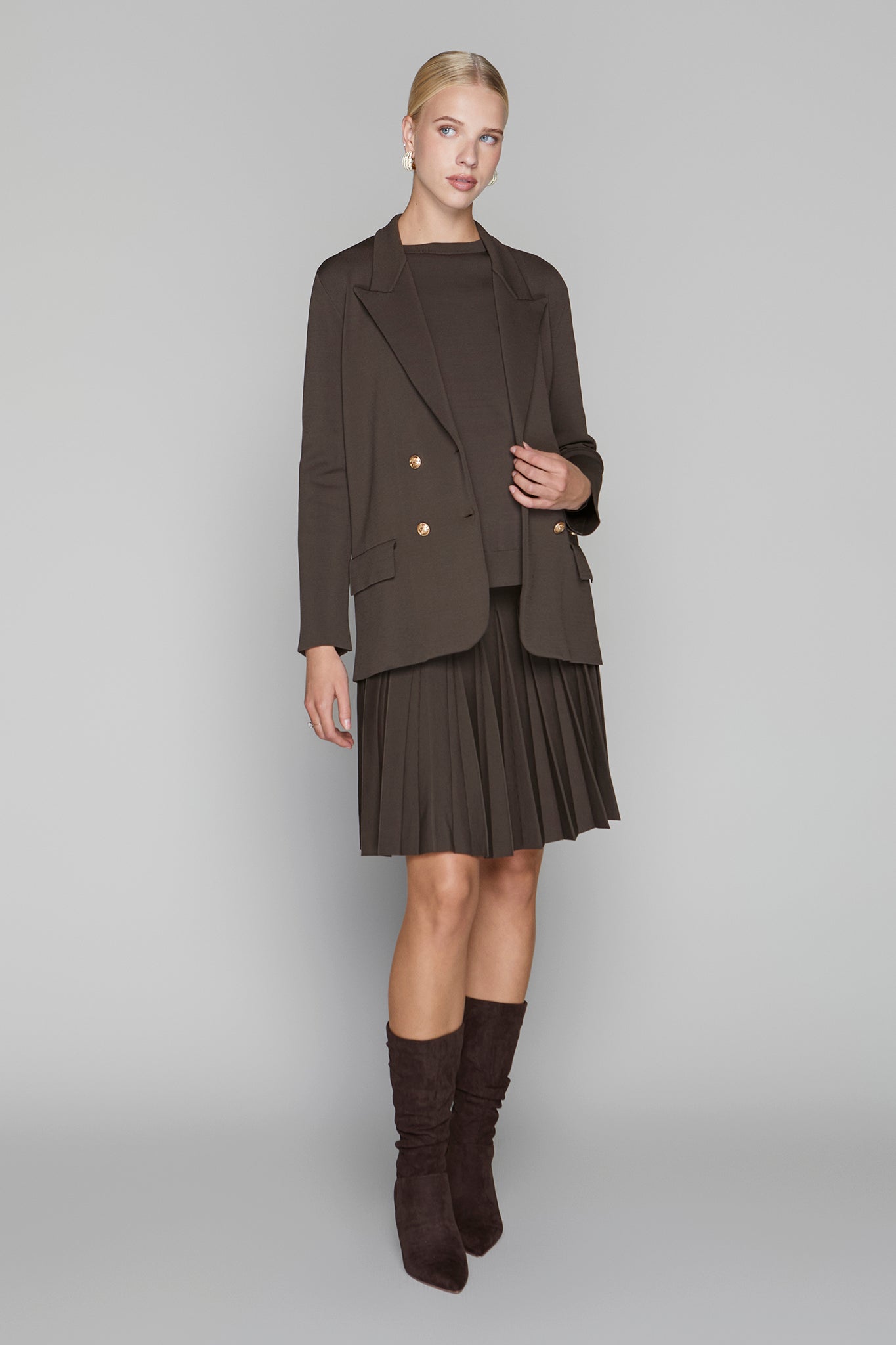 Woman wearing a brown blazer, skirt, and knee-high boots on a gray background
