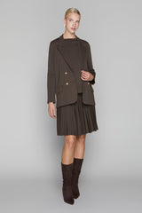 Woman wearing a brown blazer, skirt, and knee-high boots on a gray background