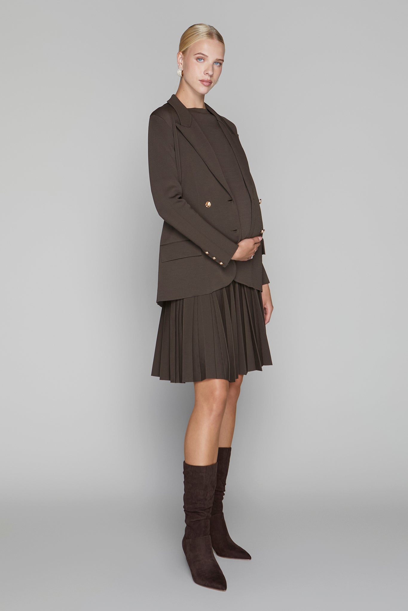 Woman wearing a brown coat, skirt, and knee-high boots on a gray background