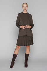 Woman wearing a brown blazer and pleated skirt set with matching boots on a gray background
