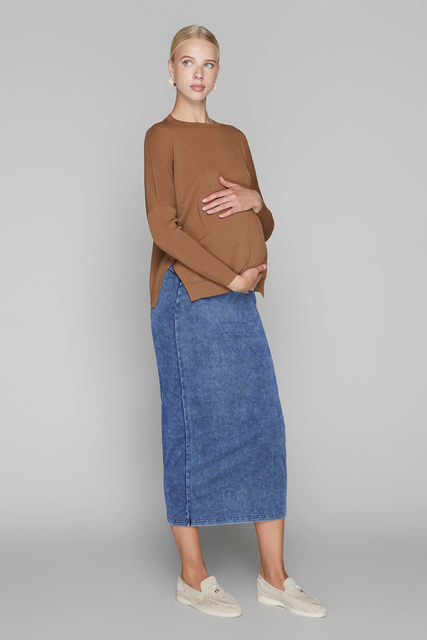 Woman wearing a brown sweater and blue denim skirt on a gray background