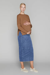 Woman wearing a brown sweater and blue denim skirt on a gray background