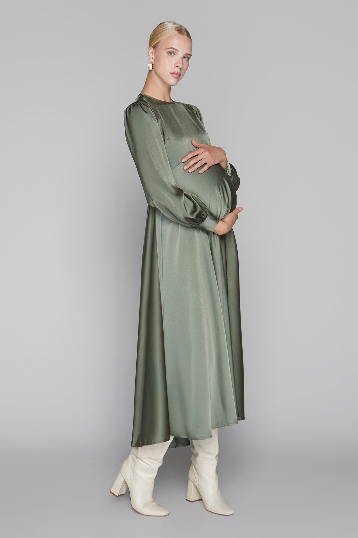Woman wearing a long green dress with white boots on a gray background
